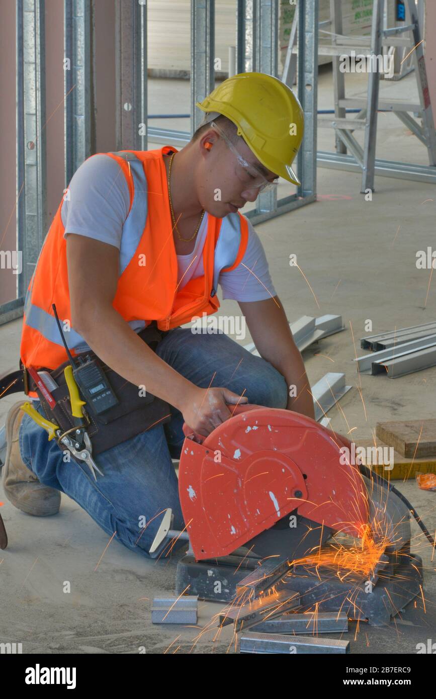 Tradesman cutting with a metal saw at work on a new architectural project, wearing high visibility shirt, boots, helmet, glasses and kneee pads. Stock Photo