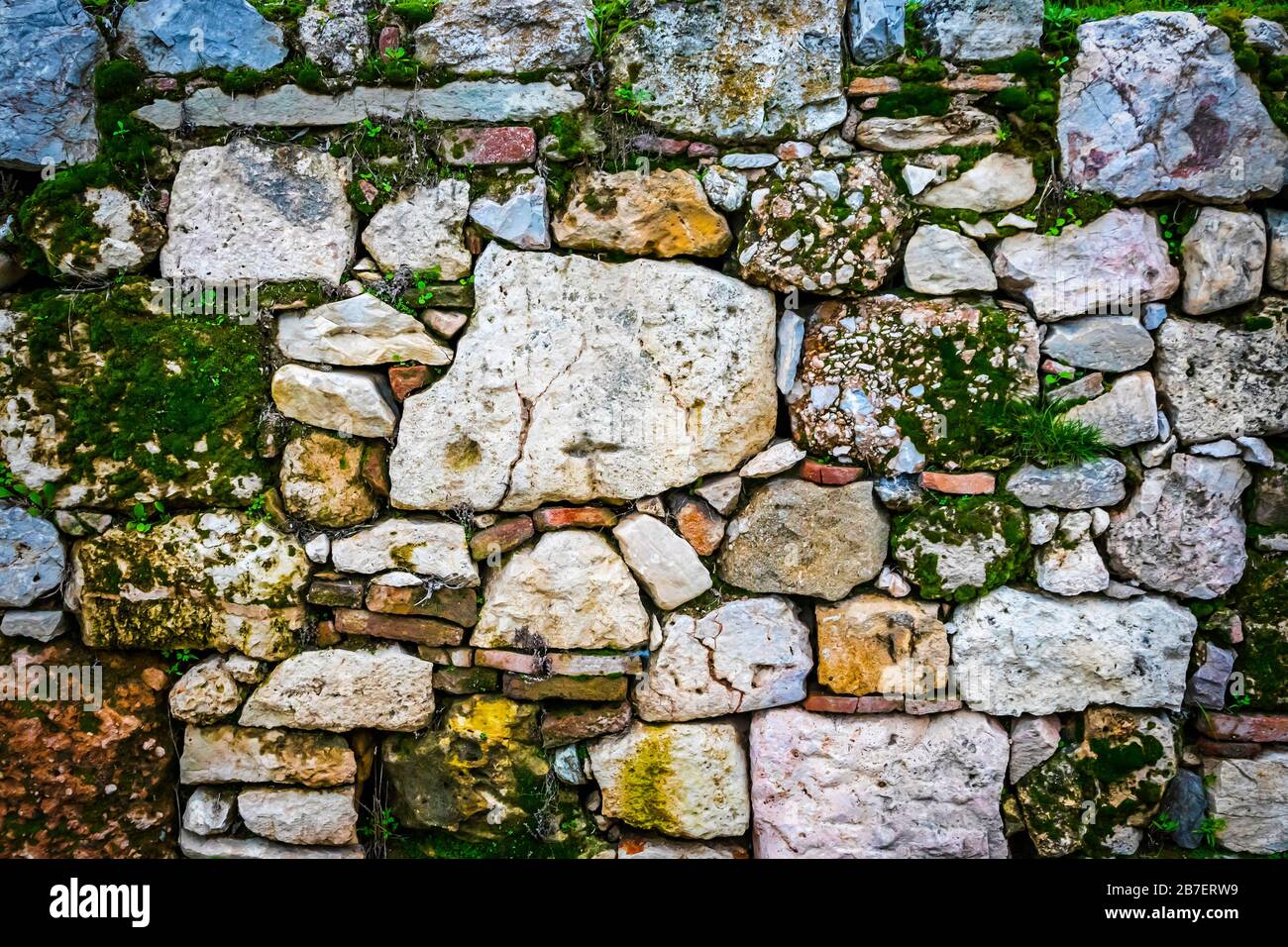 Ancient old vintage wall made of natural rocks with plants between