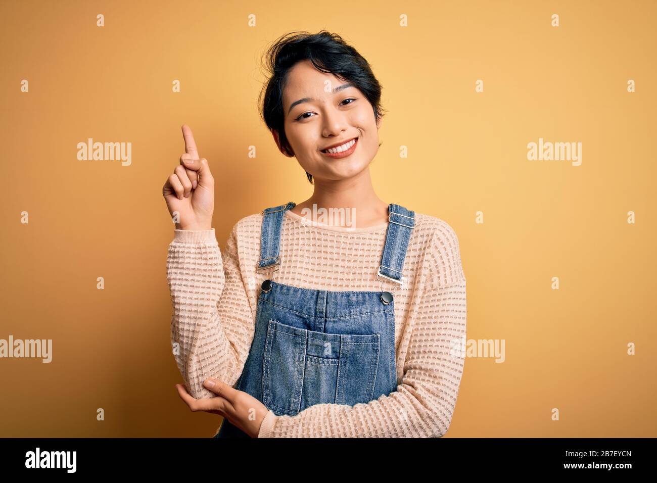 Young beautiful asian girl wearing casual denim overalls over isolated ...
