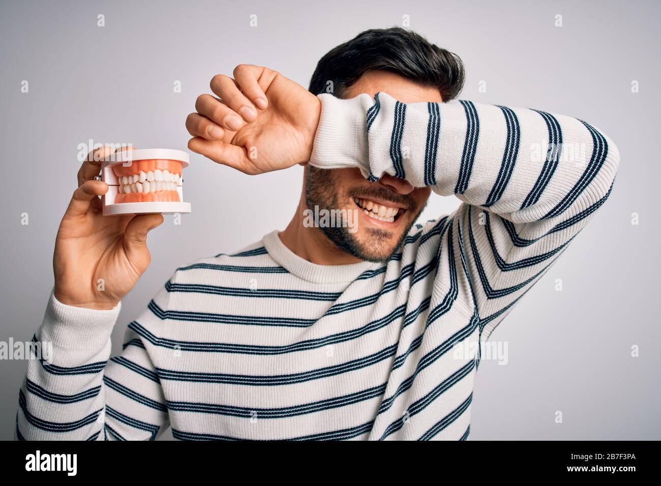 young-handsome-man-with-beard-holding-plastic-denture-teeth-over-white
