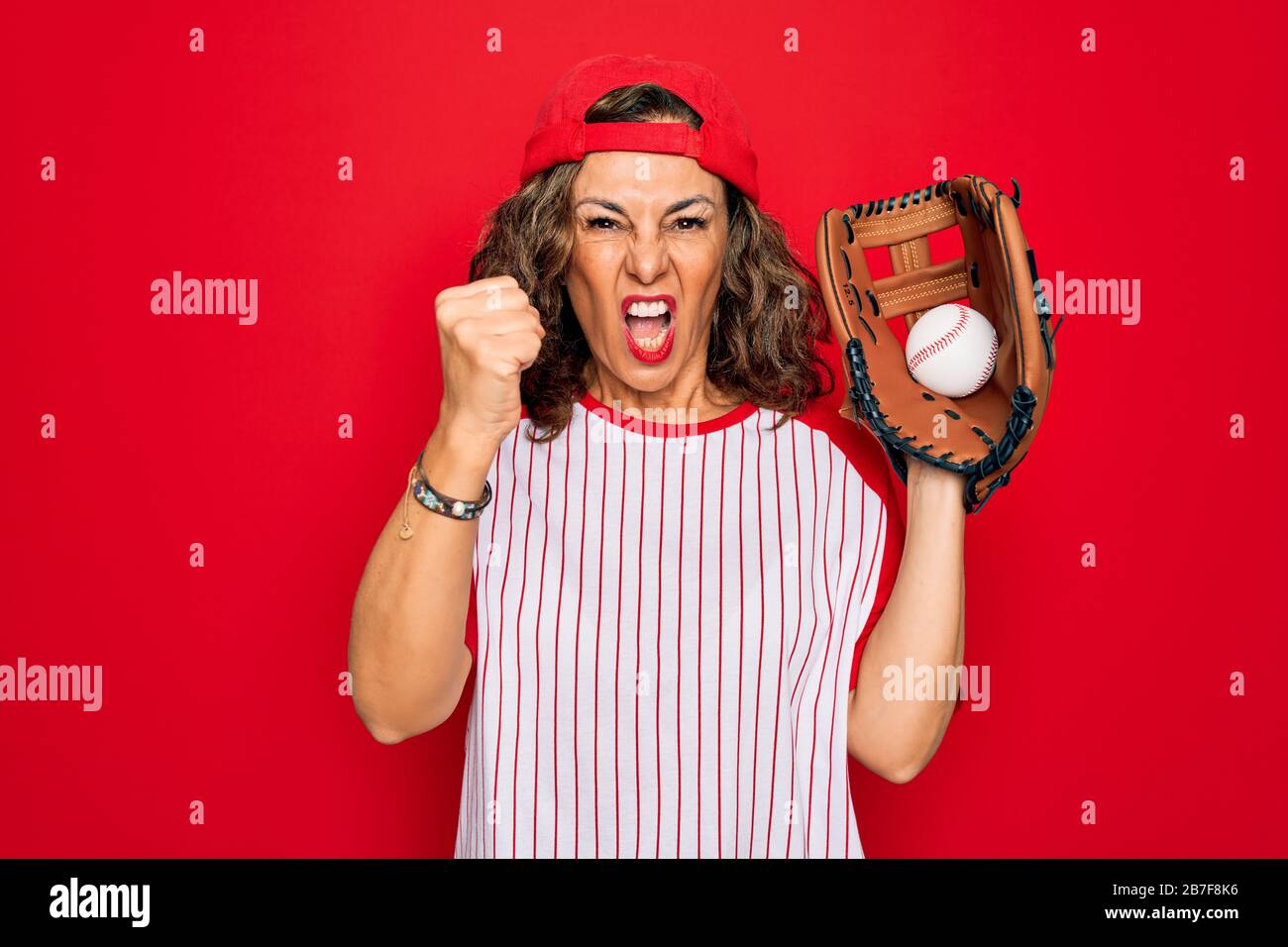 Shouting Baseball Middle age senior woman wearing baseball equiment, ball and glove over ...