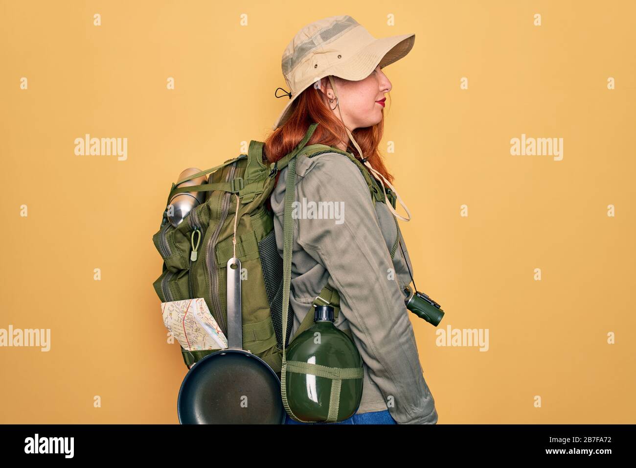 Young redhead backpacker woman hiking wearing backpack and hat over ...