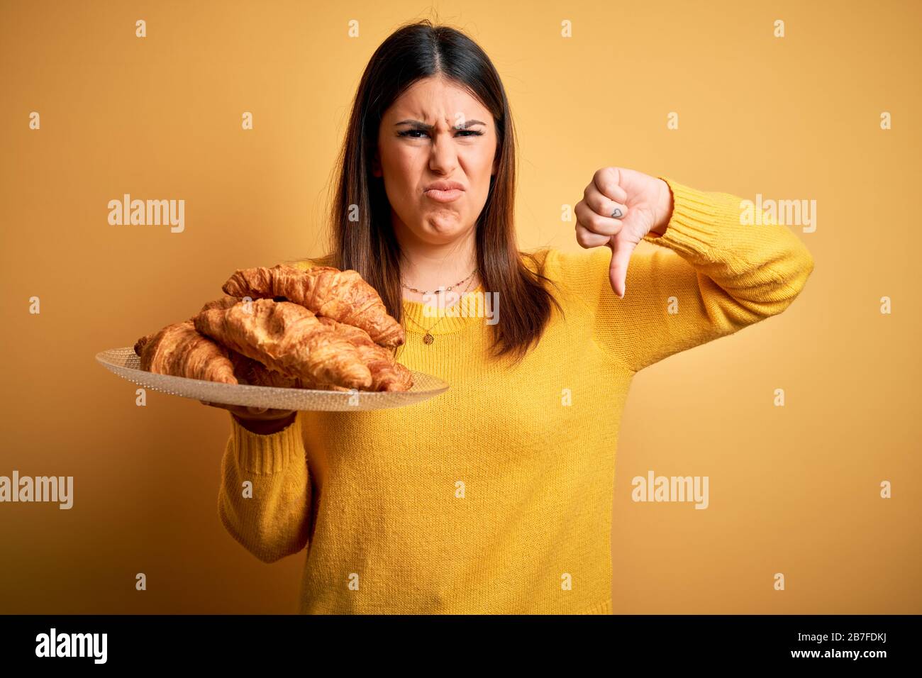 Young beautiful woman holding french croissant pastry over yellow ...