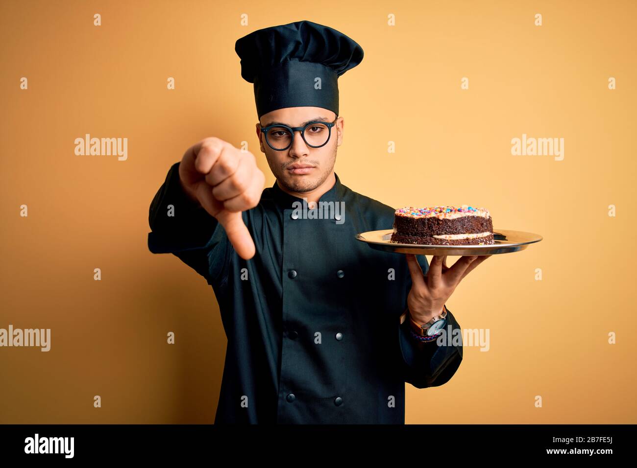 Young brazilian baker man wearing cooker uniform and hat holding tray ...