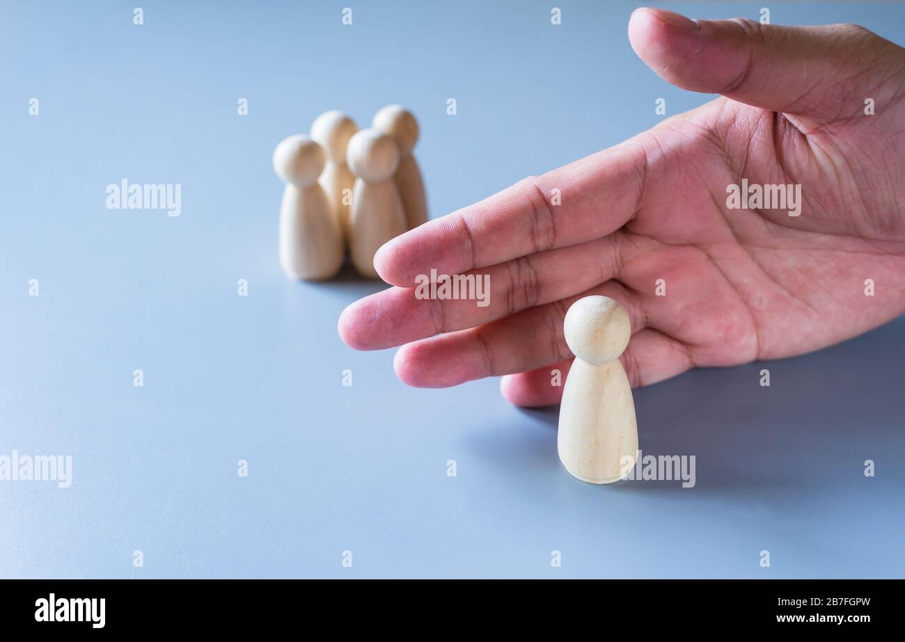 Human hand prevents a wooden doll from its group represent to self isolation or social distancing concept Stock Photo
