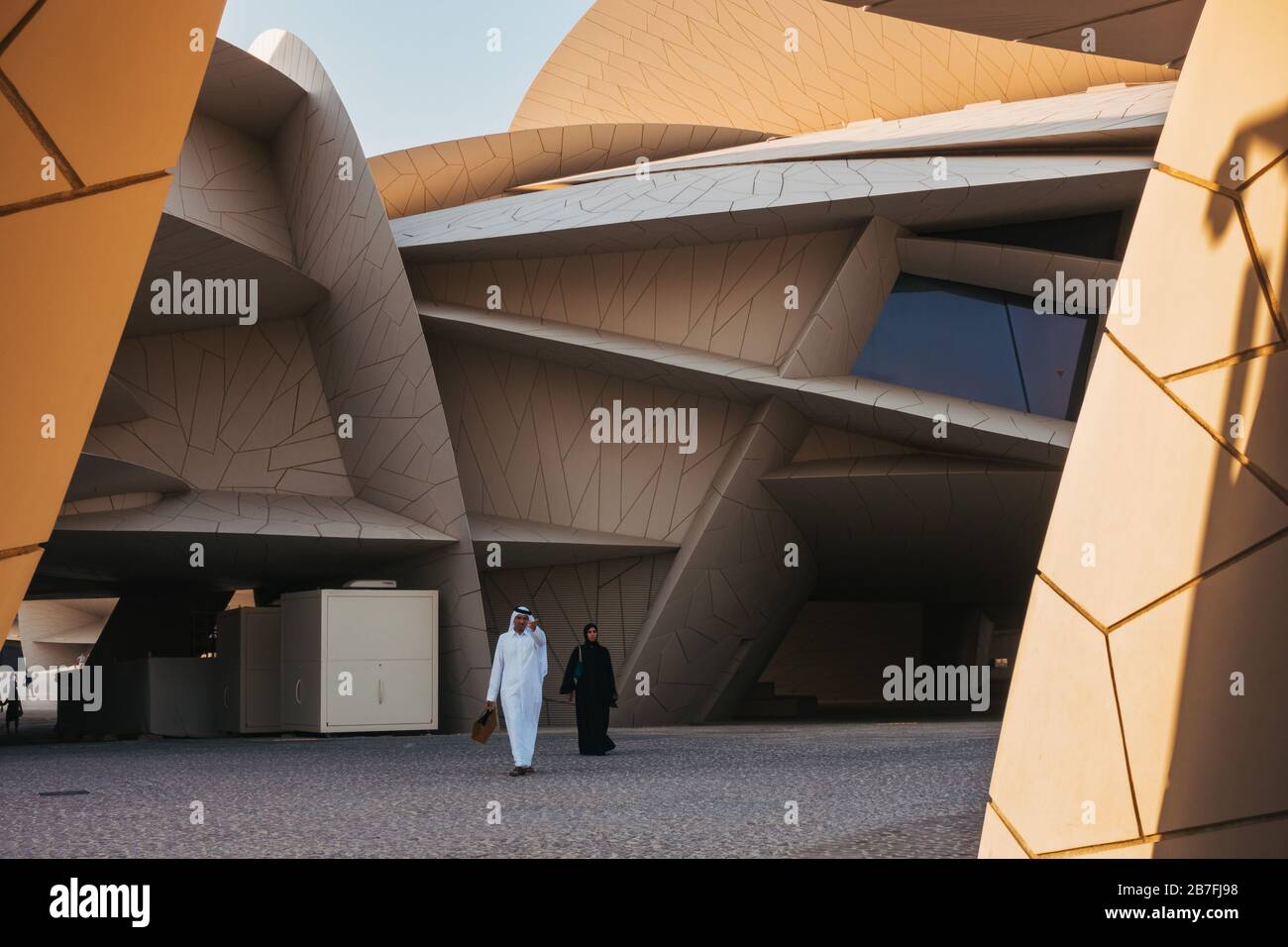 A Muslim man and woman leave the National Museum of Qatar in Doha. Voted by TIME as one of the World's Greatest Places to Visit in 2019 Stock Photo