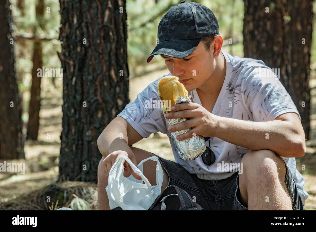 Young traveler in a cp with backpack and hiking stick sits on a stone ...