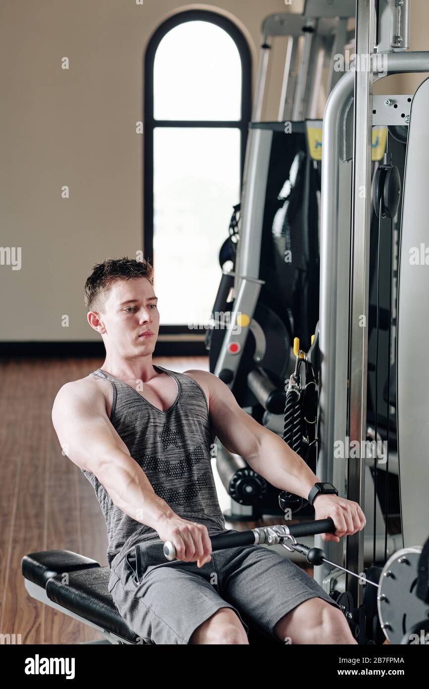 Serious handsome young bodybuilder concentrated on doing exercise in