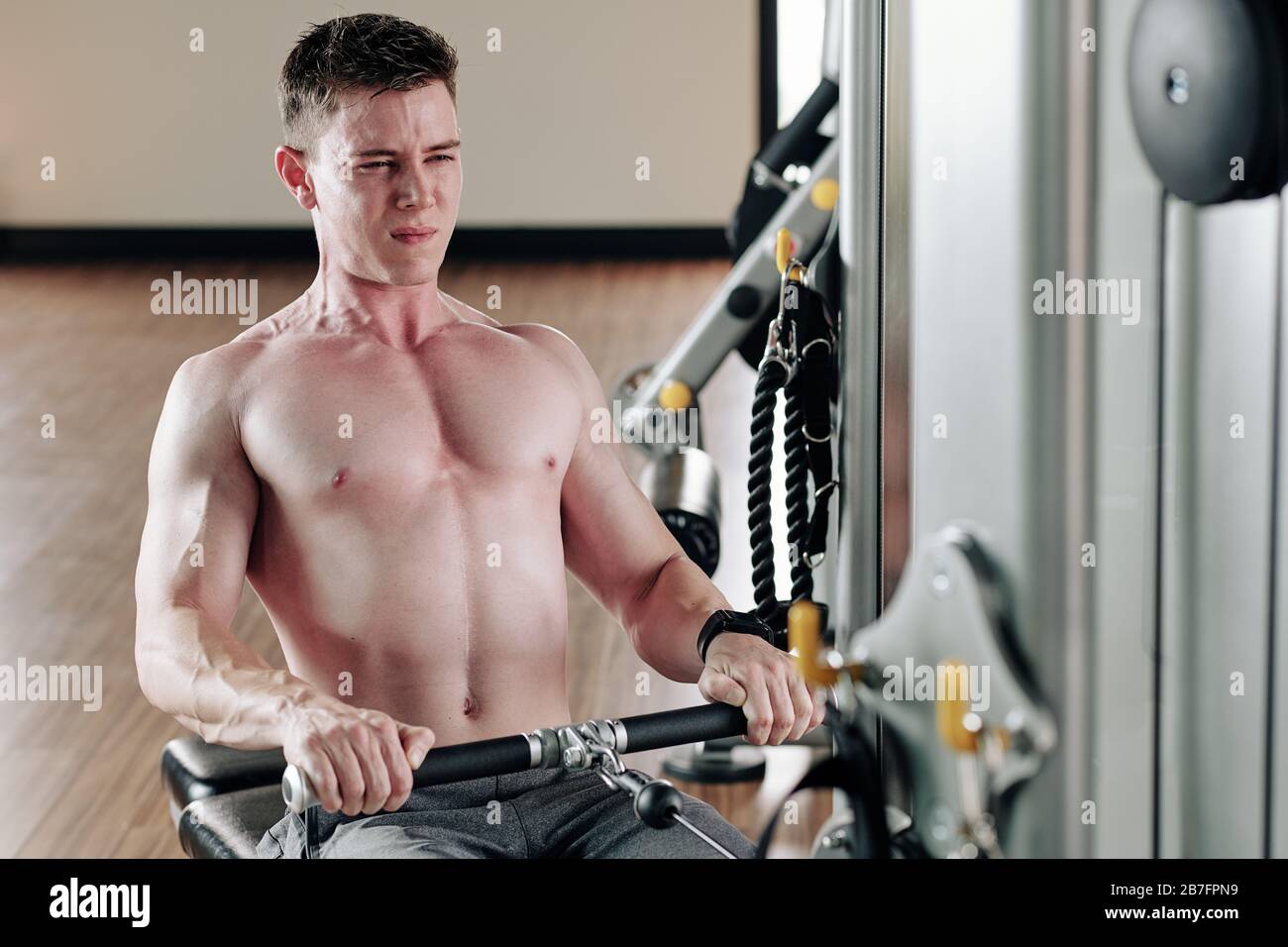 Shirtless fit young man pulling cable of rowing machine when having ...