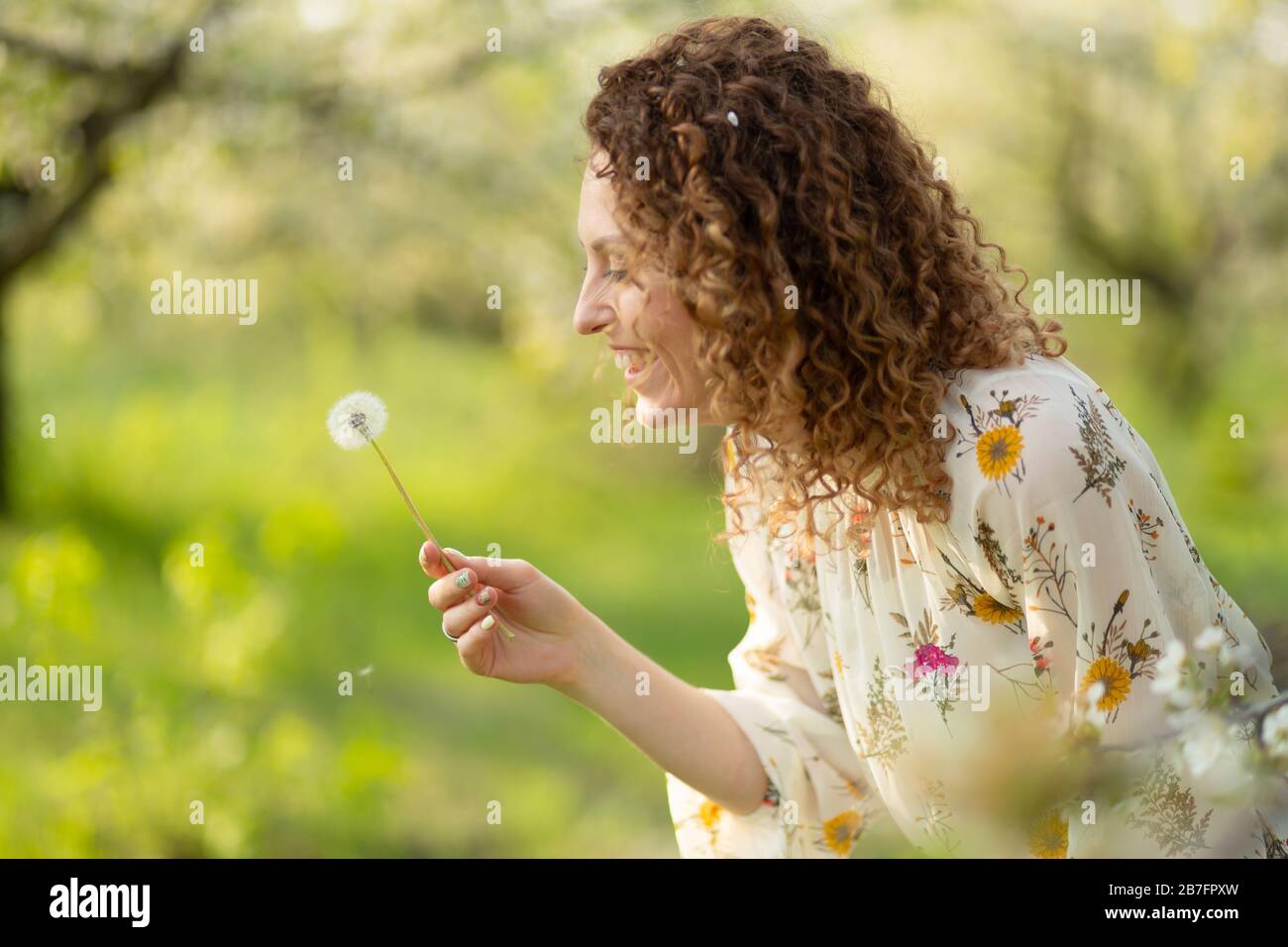 Pretty girl blowing dandelion in summer park. Green grass