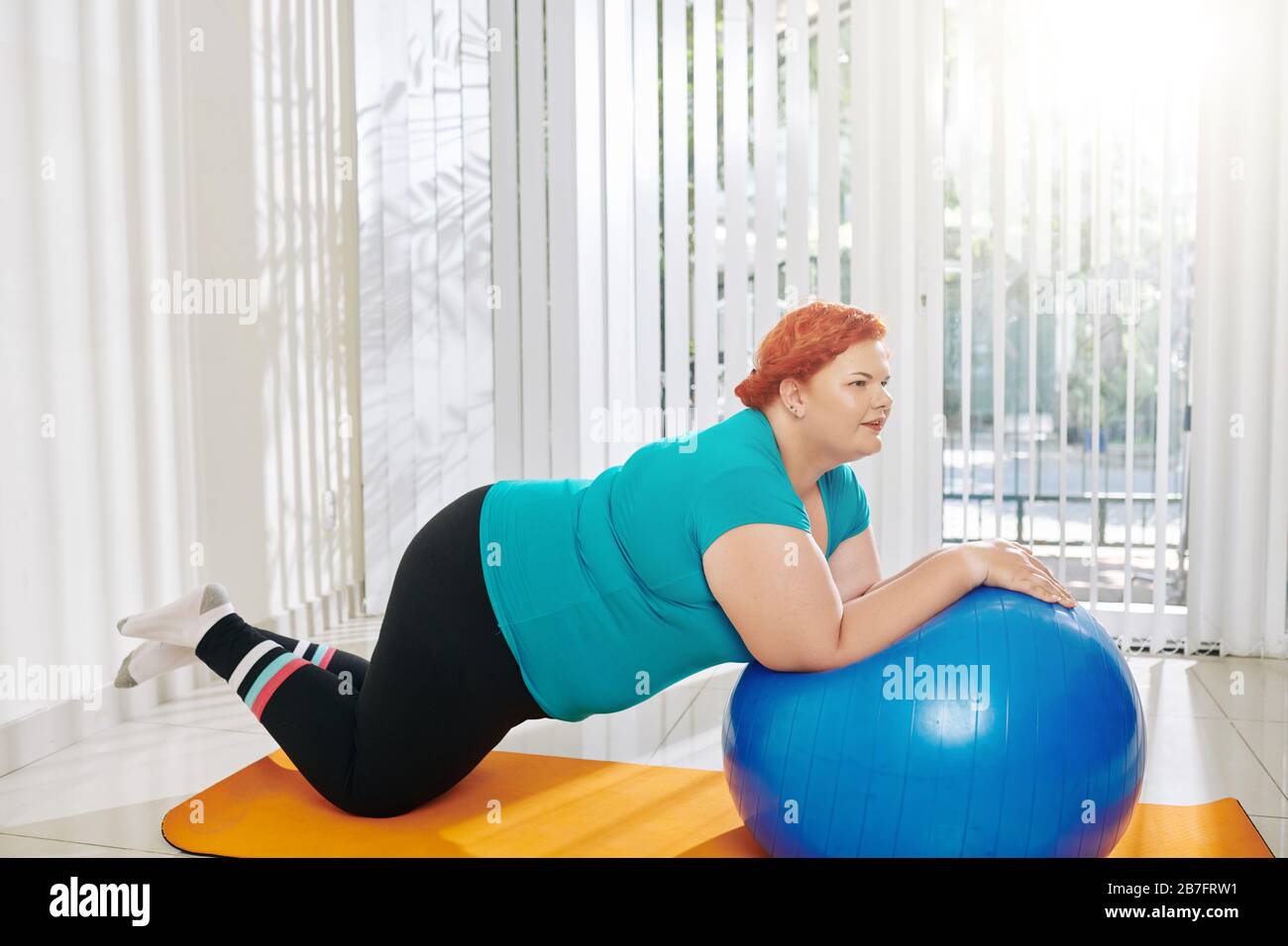Overweight young woman doing exercises with fitness ball at fitness