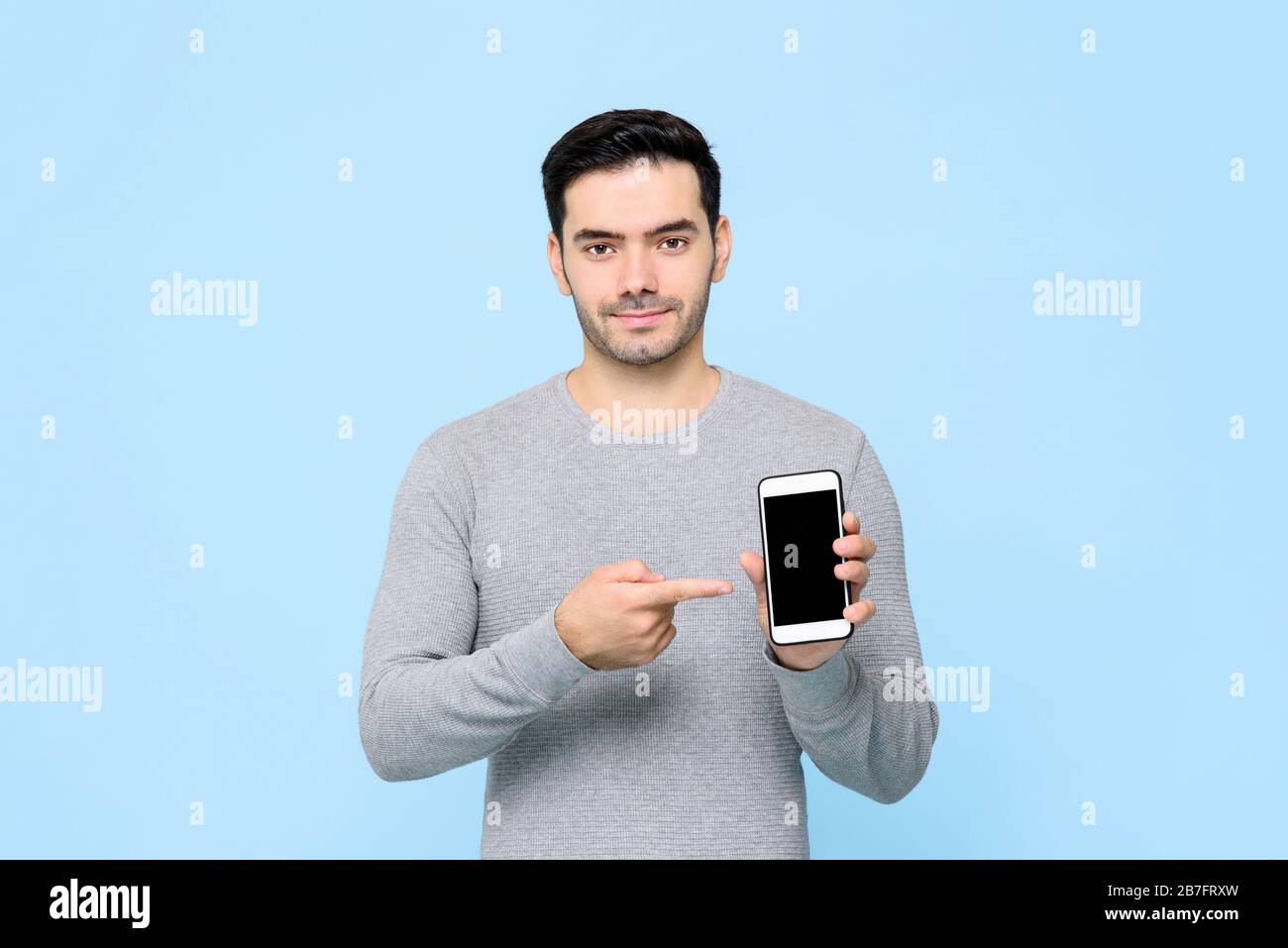 Young handsome man pointing to his mobile phone in hand isolated on light blue background Stock Photo