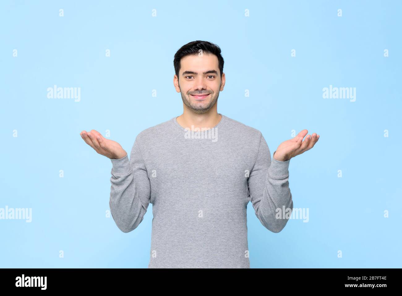 Half body portrait of smiling man in gray t-shirt with open hand gesture in light blue studio background Stock Photo