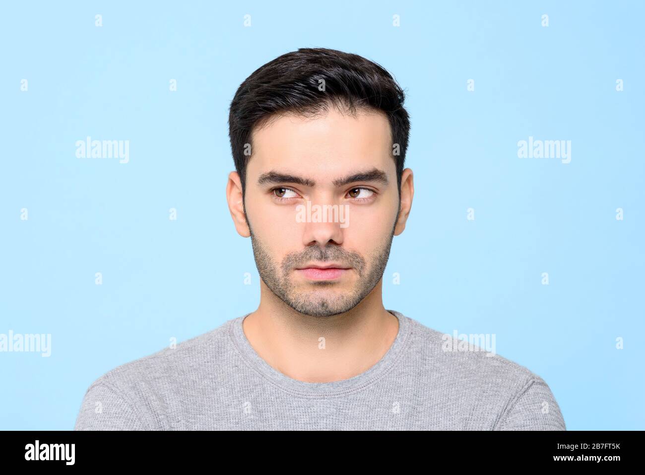 Close up portrait of handsome man thinking with eyes looking sideways isolated on blue studio background Stock Photo