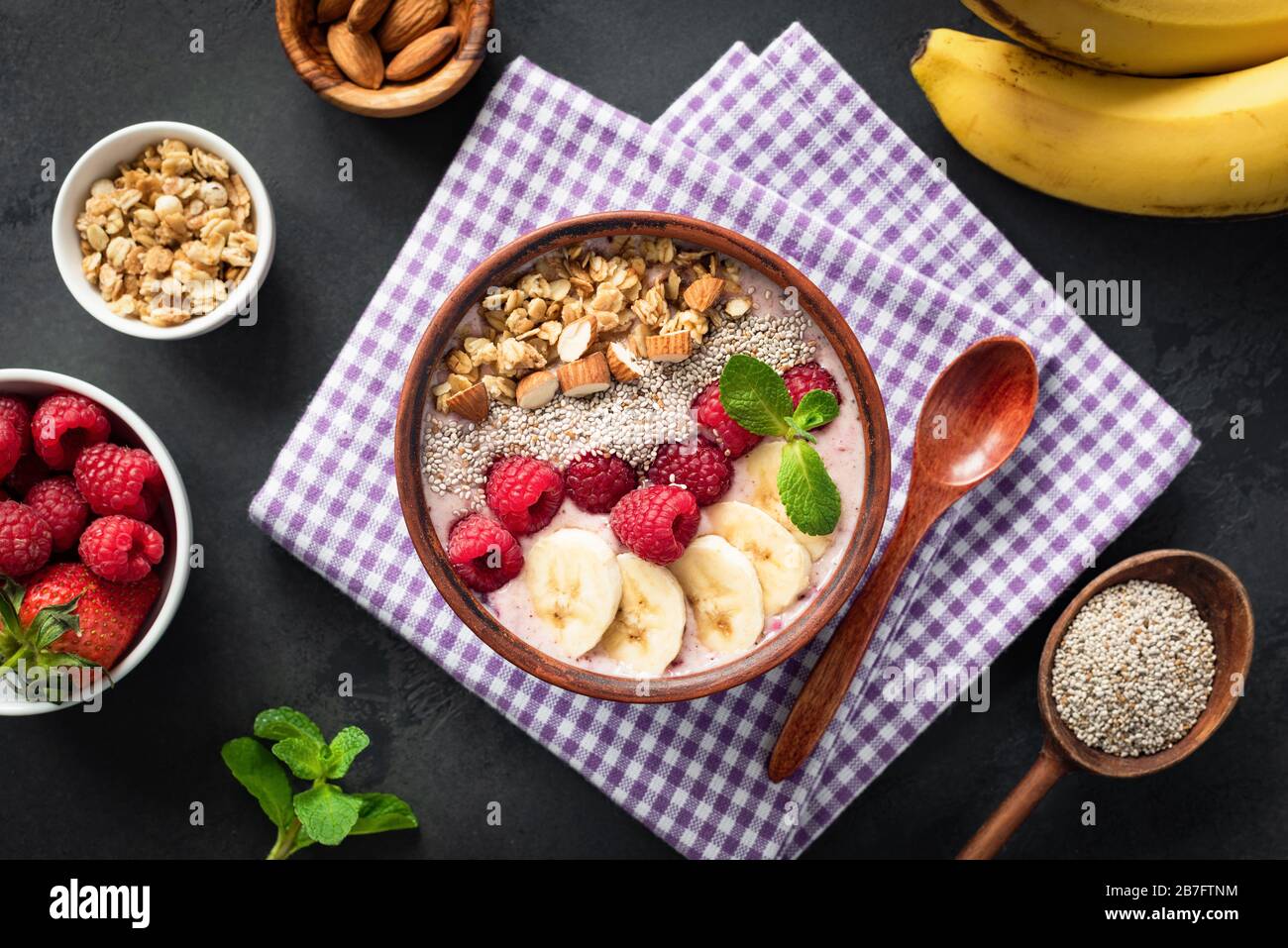 Pink smoothie bowl with raspberry banana chia seeds almonds and granola on black background. Healthy food clean eating concept. Fruit superfood smooth Stock Photo