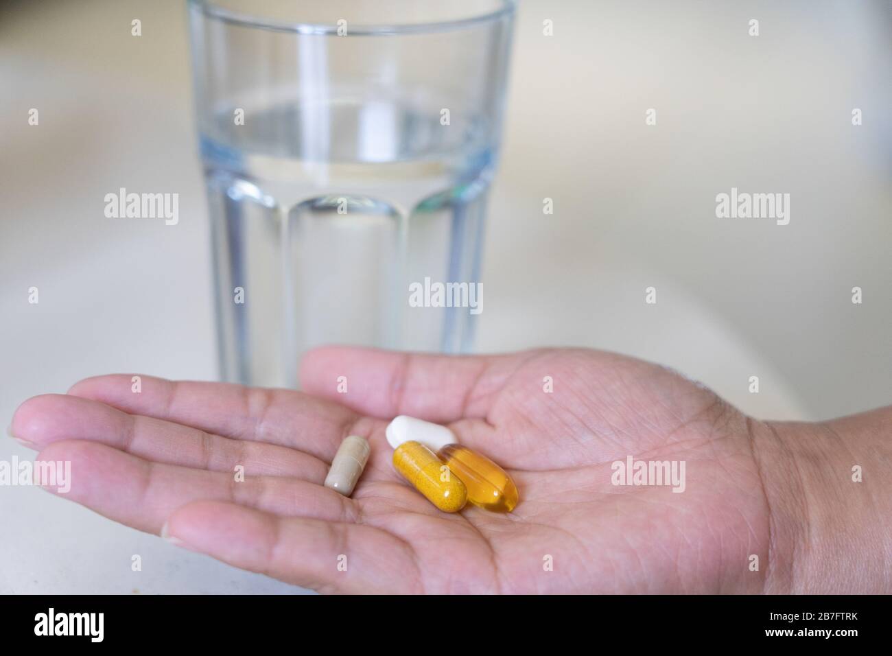 A woman with a selection of natural health supplements in the palm of her hand ready to take with a glass of water Stock Photo