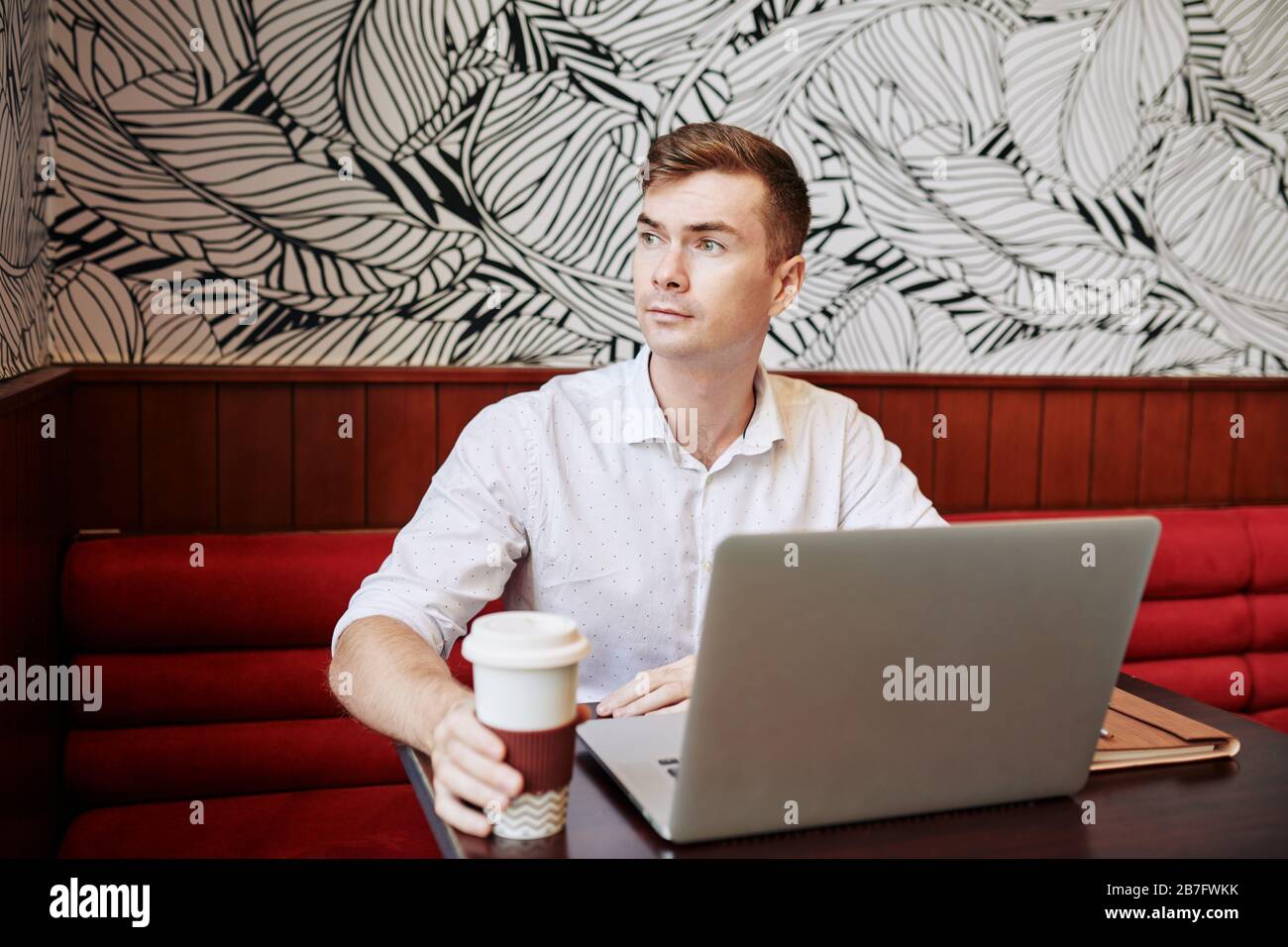 Portrait of pensive handsome young man drinking coffee when working in cafe Stock Photo