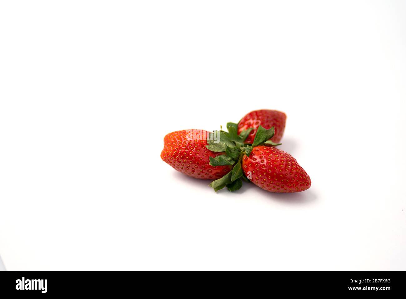 Three ripe fresh red strawberries with green leaves isolated on a white ...
