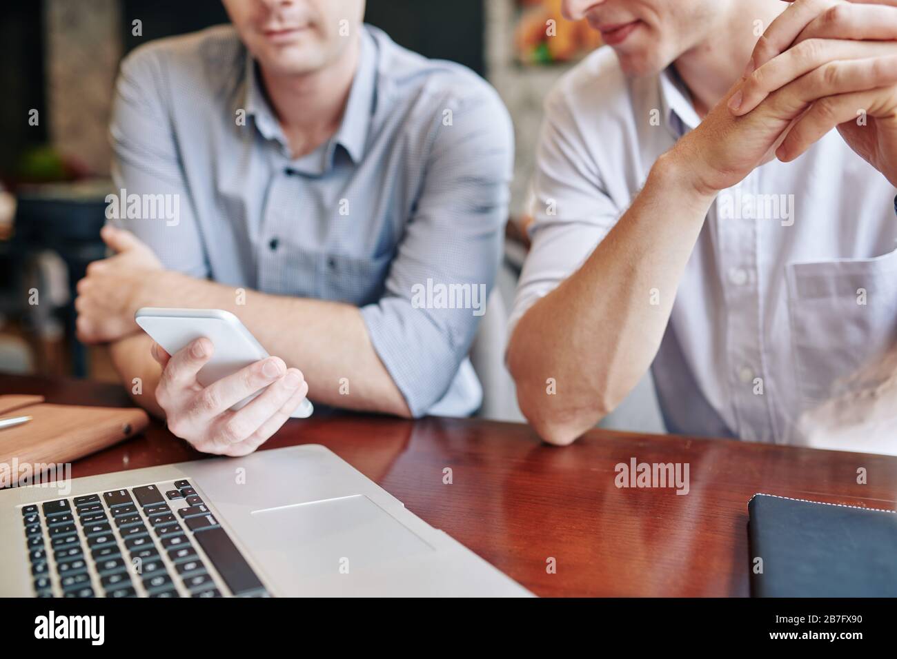 Young businessman showing text message or mobile application on smartphone screen to colleague at meeting Stock Photo