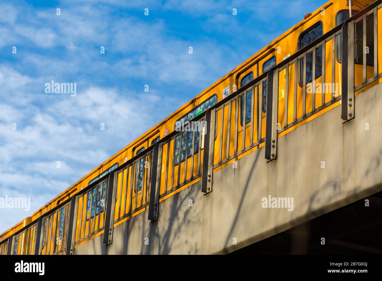 Yellow U-Bahn train crossing a bridge at Böcklerpark (Close to Prinzenstraße subway station). Composition of metro with blue sky. Symbol for tourism, Stock Photo