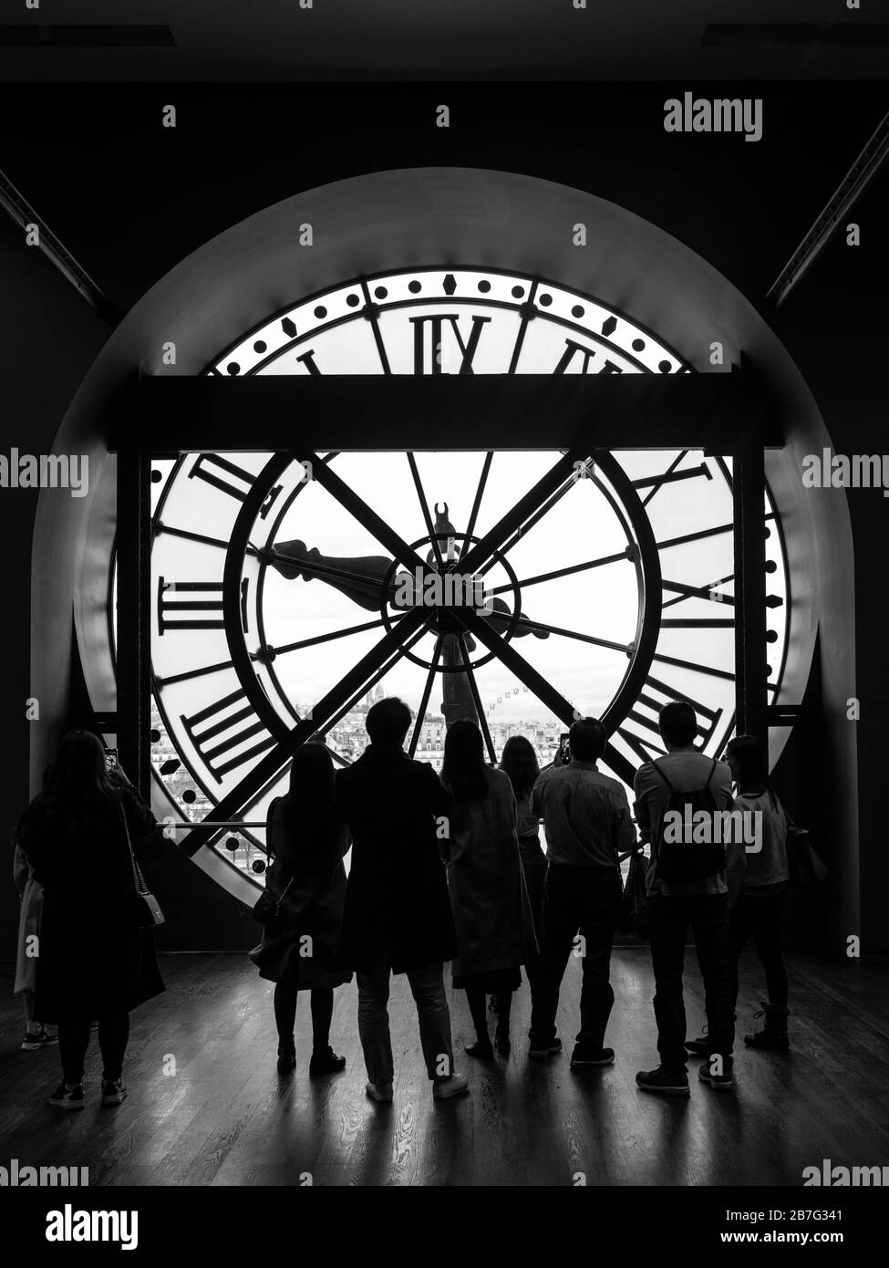 Paris, France - December 23, 2018: Visitors observe a panoramic view thought the glass clock in the Musee d Orsay in Paris, France. Black and white ph Stock Photo