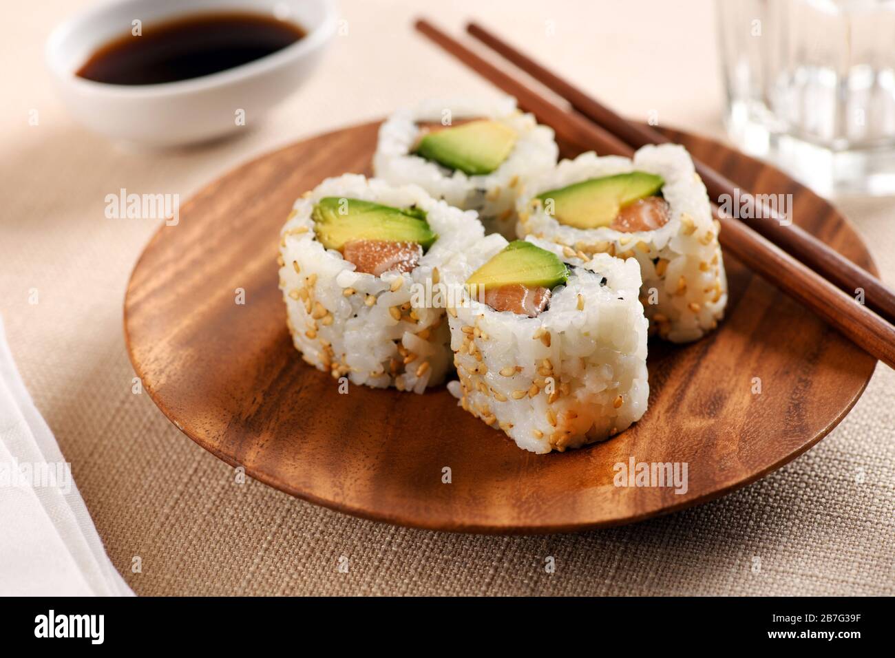 Four traditional uramaki sushi rolls with fresh raw salmon, avocado pear, nori and rice on a circular wood tray with chopsticks served at table on a l Stock Photo