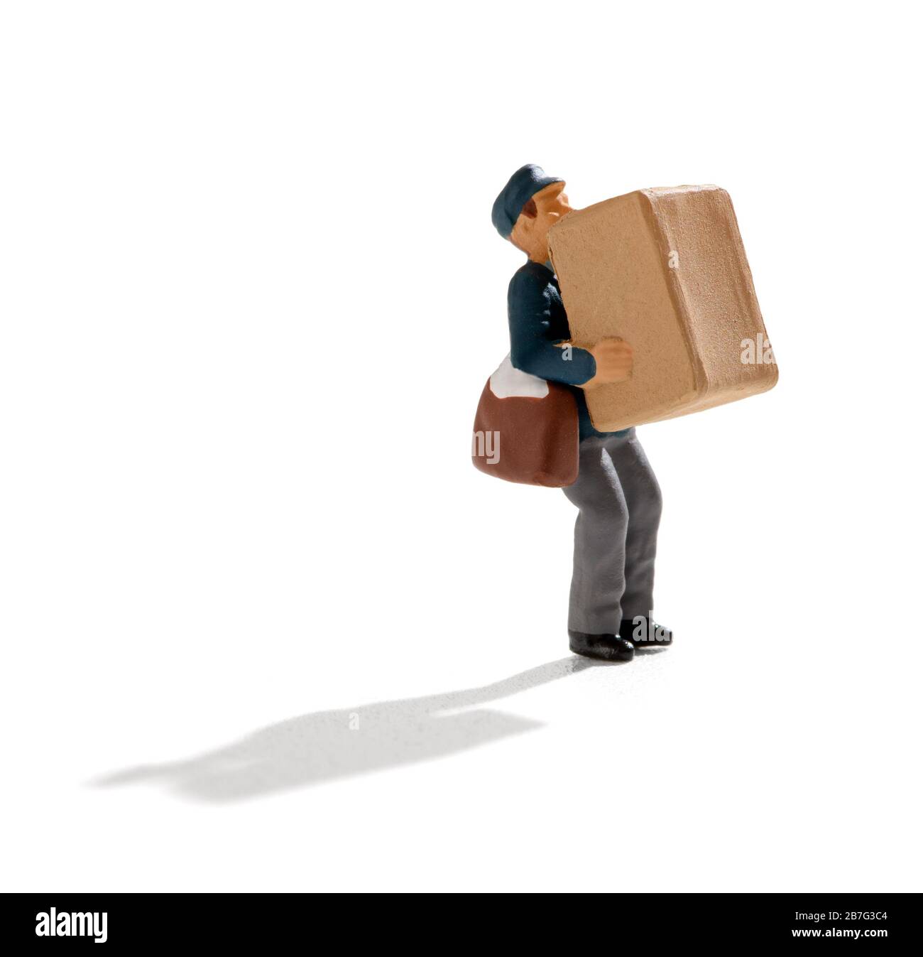 Miniature postman with his satchel of letters over his shoulder carrying a large brown box for delivery over white with shadow Stock Photo
