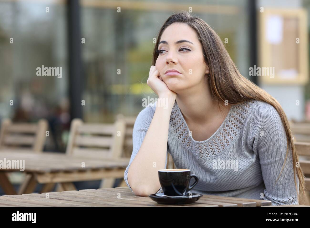 Bored girl looking to the side sitting alone on a restaurant terrace Stock Photo
