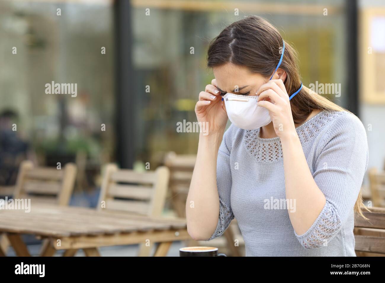 Serious woman putting on protective mask preventing contagion at coffee shop terrace Stock Photo