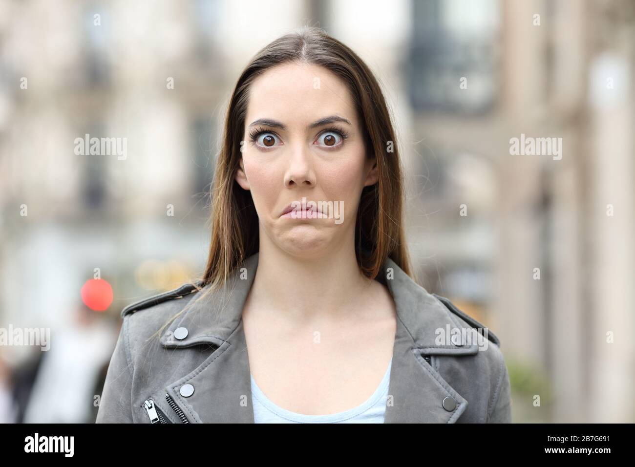 Front view portrait of a shocked young woman looking perplexed at camera on city street Stock Photo