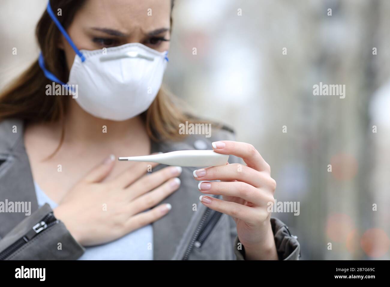 Worried sick woman with protective mask checking thermometer on street Stock Photo