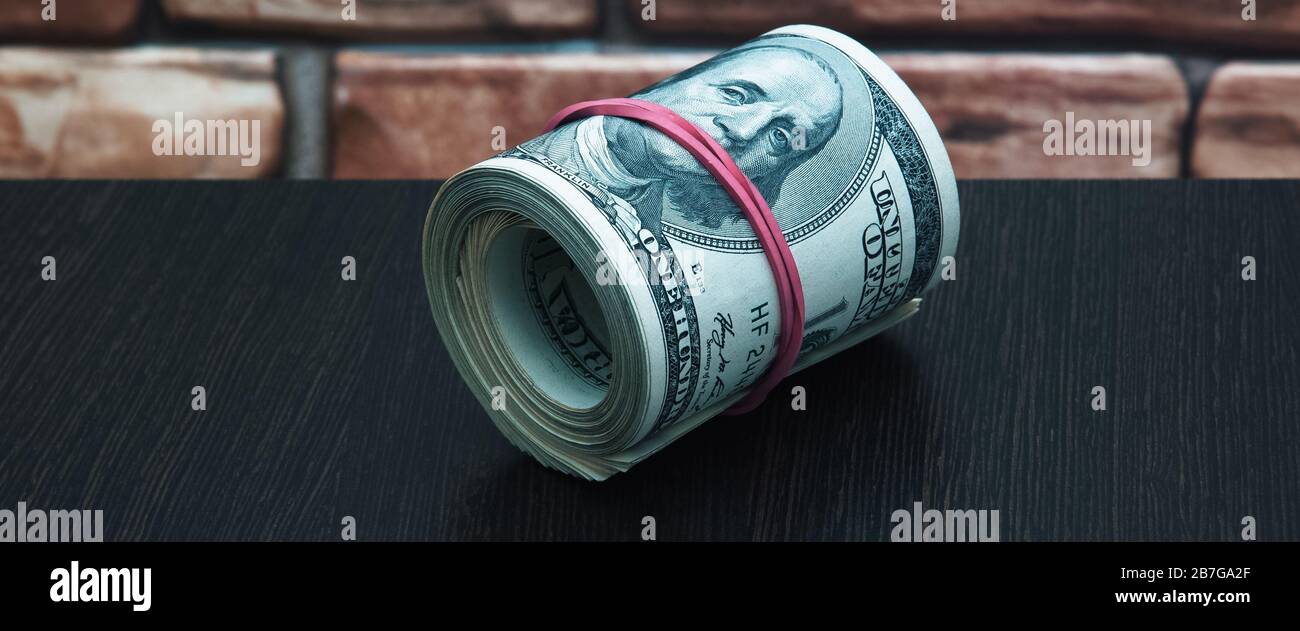 A roll of one hundred American banknotes cash close - up against a ...