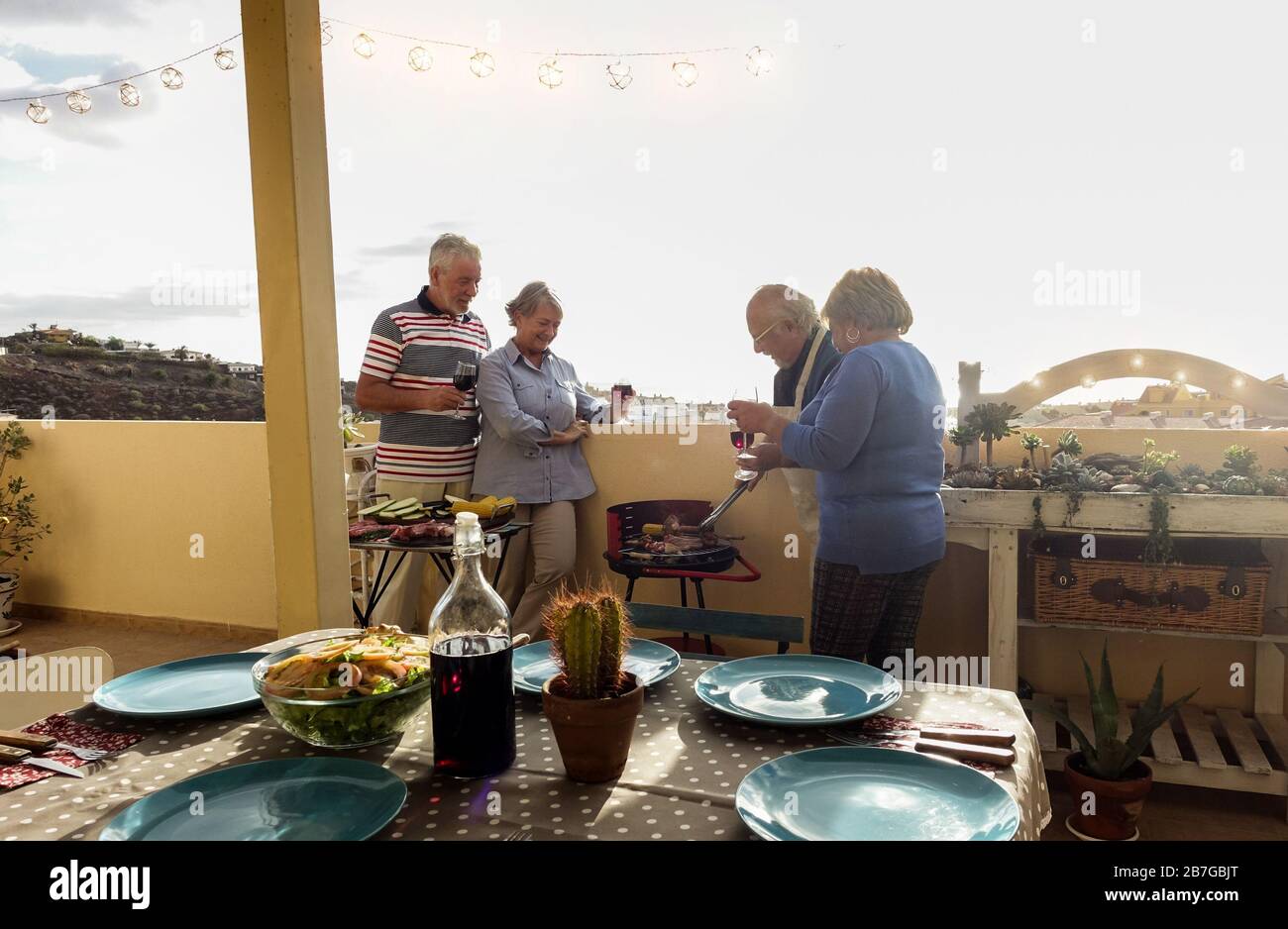 Senior happy couples eating and drinking wine at barbecue dinner outdoor - Mature people having fun dining and laughing together - Main focus on left Stock Photo