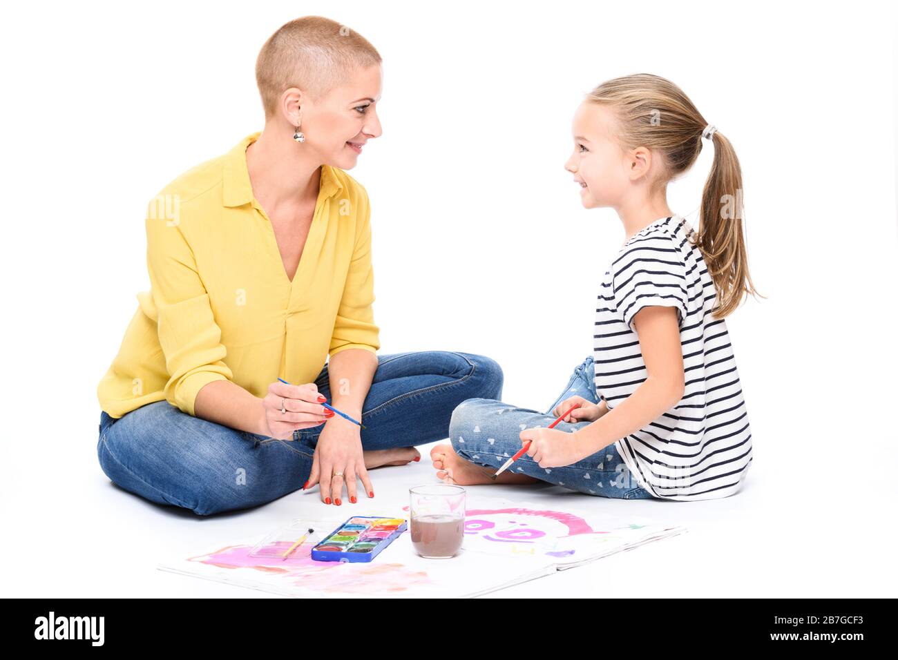 Young girl and her therapist in child occupational therapy session painting with watercolors. Child therapy concept on white background. Stock Photo
