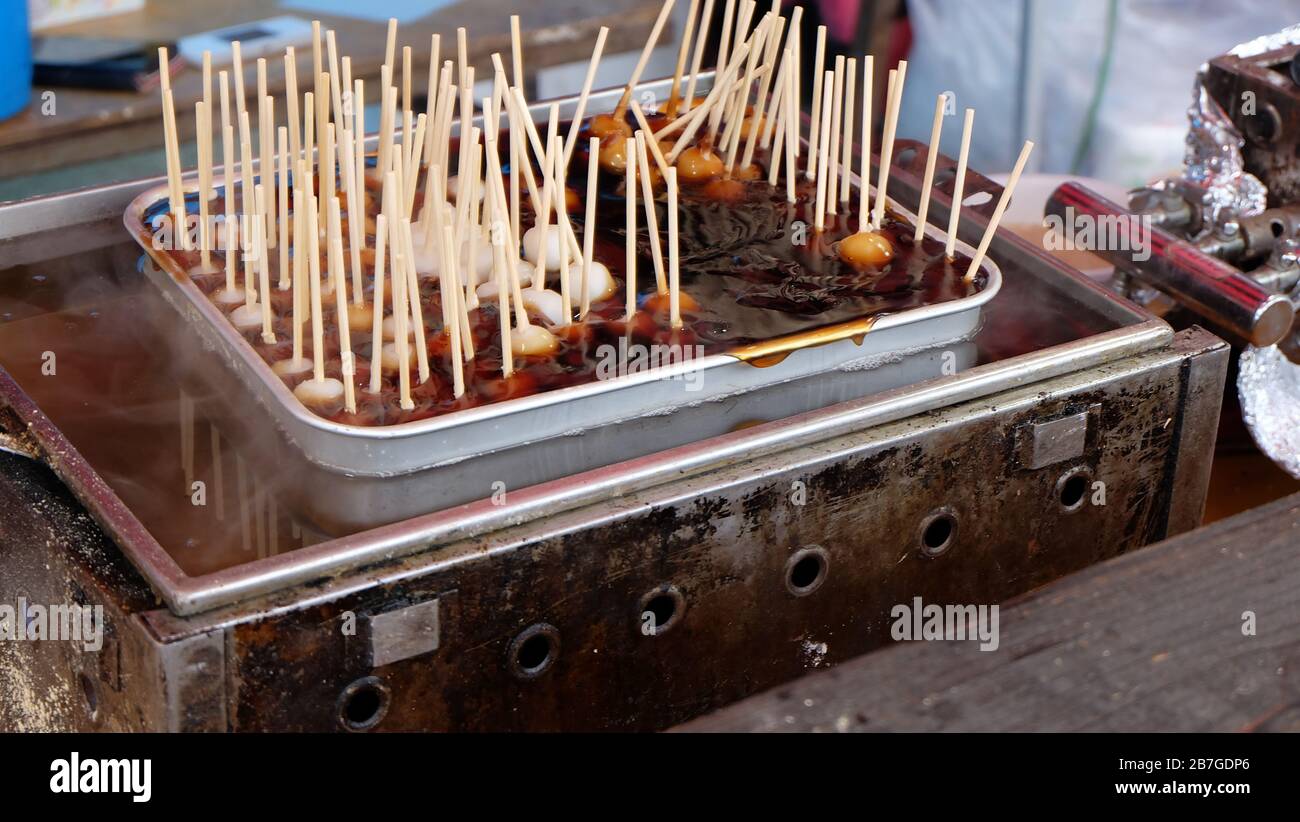 Mitarashi dango, a type of dango skewered onto sticks and covered with a sweet soy sauce glaze, soaked into a pot of sauce, ready for sale. Stock Photo