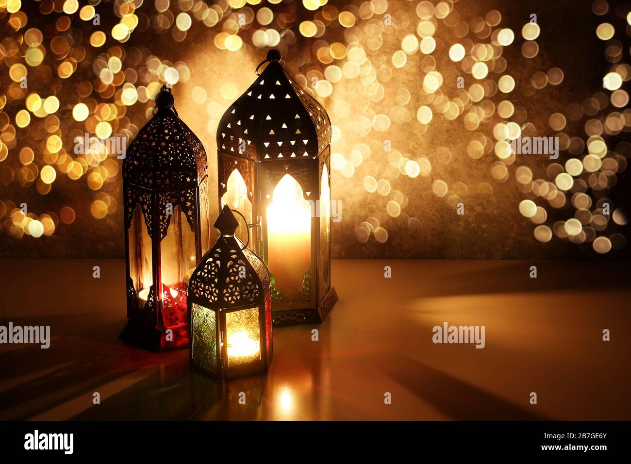 Ornamental Arabic lanterns with glittering bokeh lights. Burning candles on table glowing at night. Festive greeting card, invitation for Muslim Stock Photo