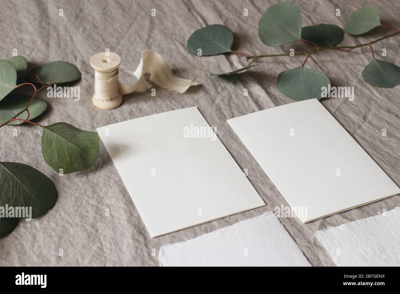 Wedding stationery mock-up scene. Blank greeting cards on linen tablecloth background with green eucalyptus tree leaves and branches and silk ribbon Stock Photo