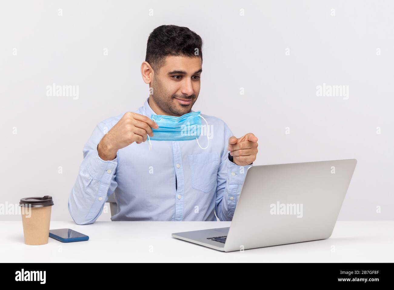 Positive office worker holding hygienic mask and pointing at laptop ...