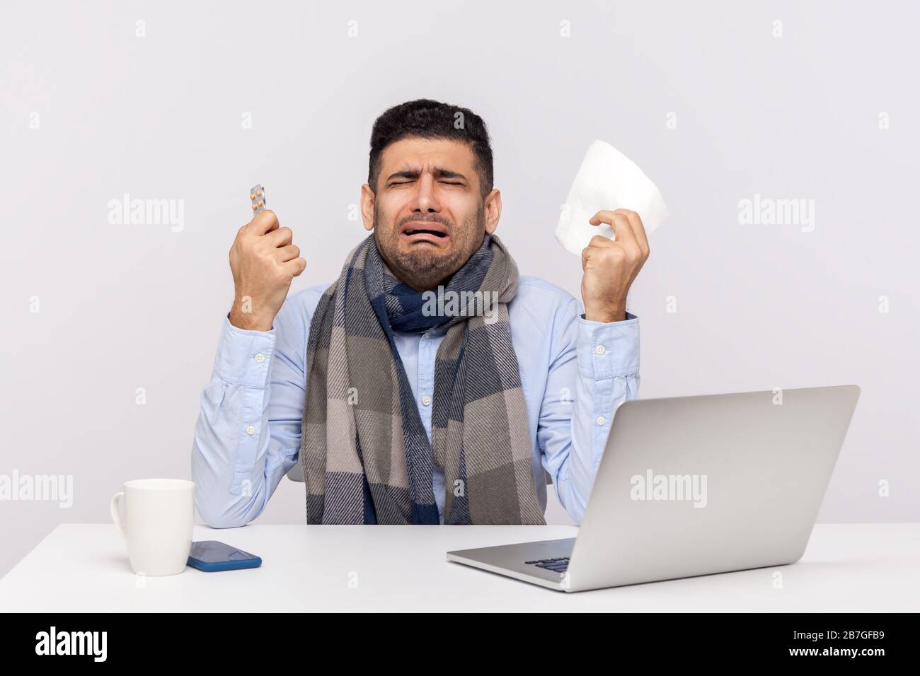 Flu-sick office worker in scarf holding pills, tissue and crying with funny expression, employee feeling unwell, panicking afraid of coronavirus infec Stock Photo