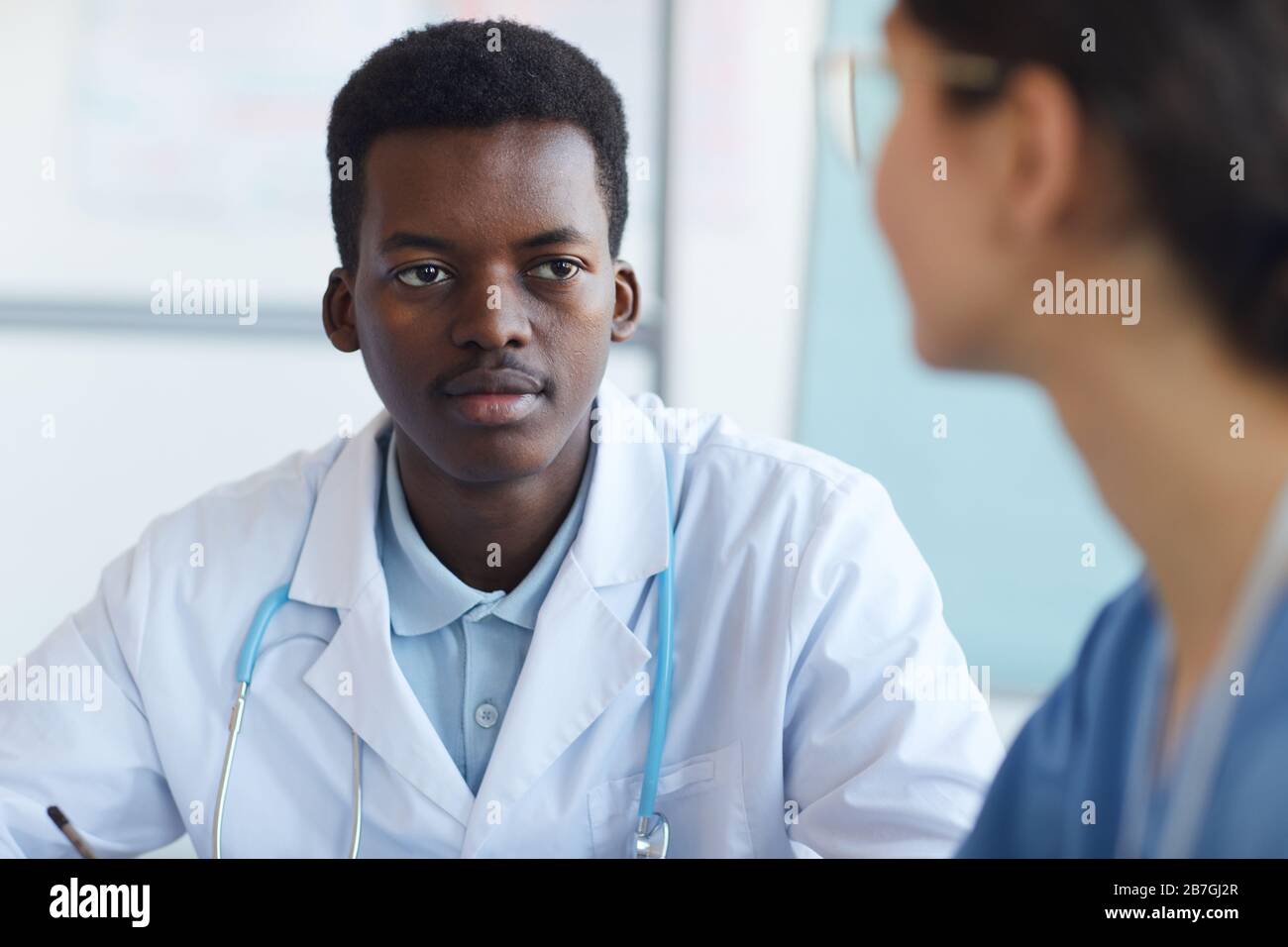 Portrait of young African-American doctor listening at colleague while sitting at meeting table, copy space Stock Photo