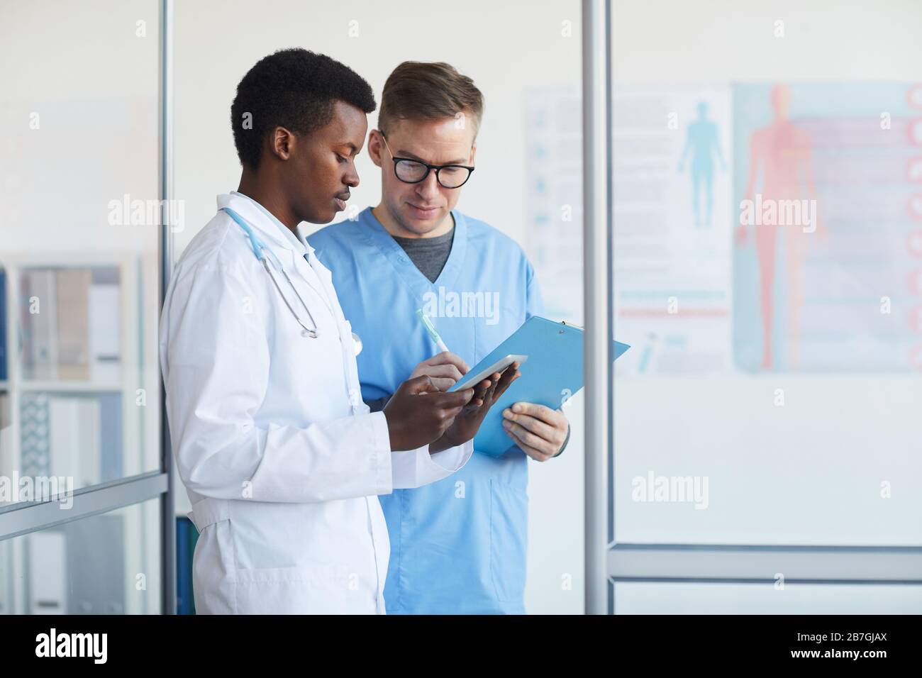 Waist up portrait of young African-American doctor talking to supervisor in medical office interior, copy space Stock Photo