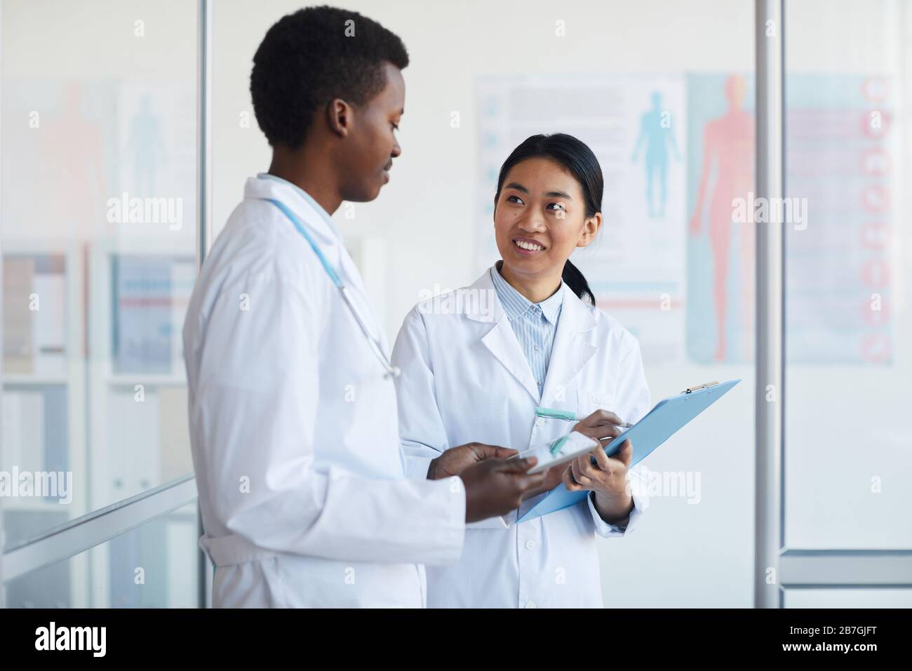 Waist up portrait of young African-American doctor talking to female colleague in medical office interior, copy space Stock Photo