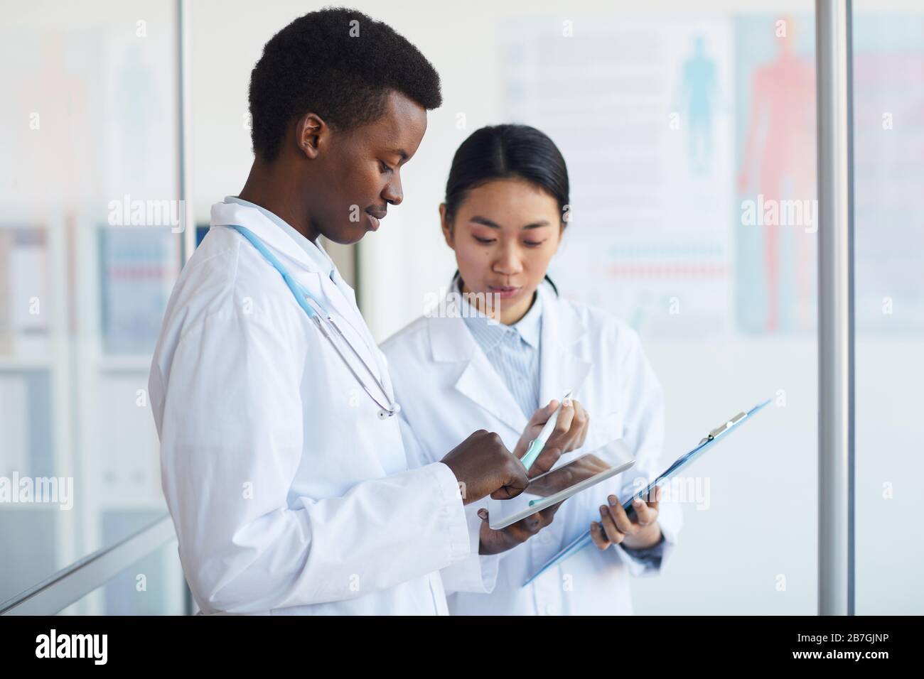 Side view portrait of young African-American doctor talking to female colleague in medical office interior, copy space Stock Photo