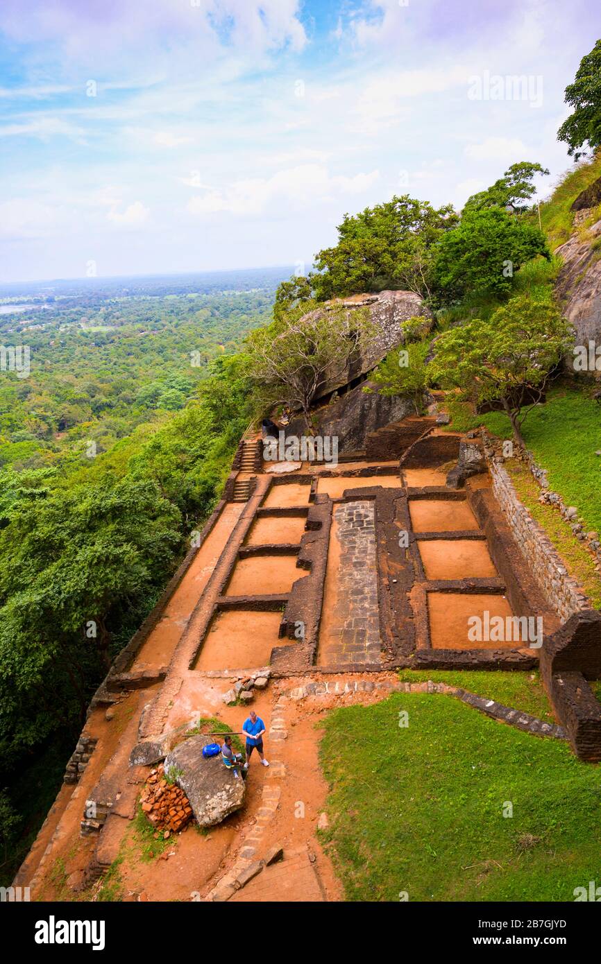 Asia Sri Lanka Sigiriya Rock terraced garden ruins granite boulder secret passage stairs steps red earth bricks grass trees tourists Stock Photo