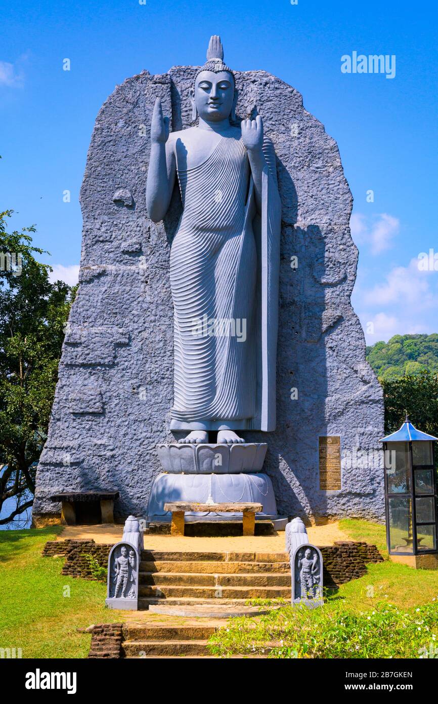 South Asia Sri Lanka giant modern grey grey stone sculpture of Buddha Guard Stone steps stairs by irrigation reservoir altar small white statue Stock Photo