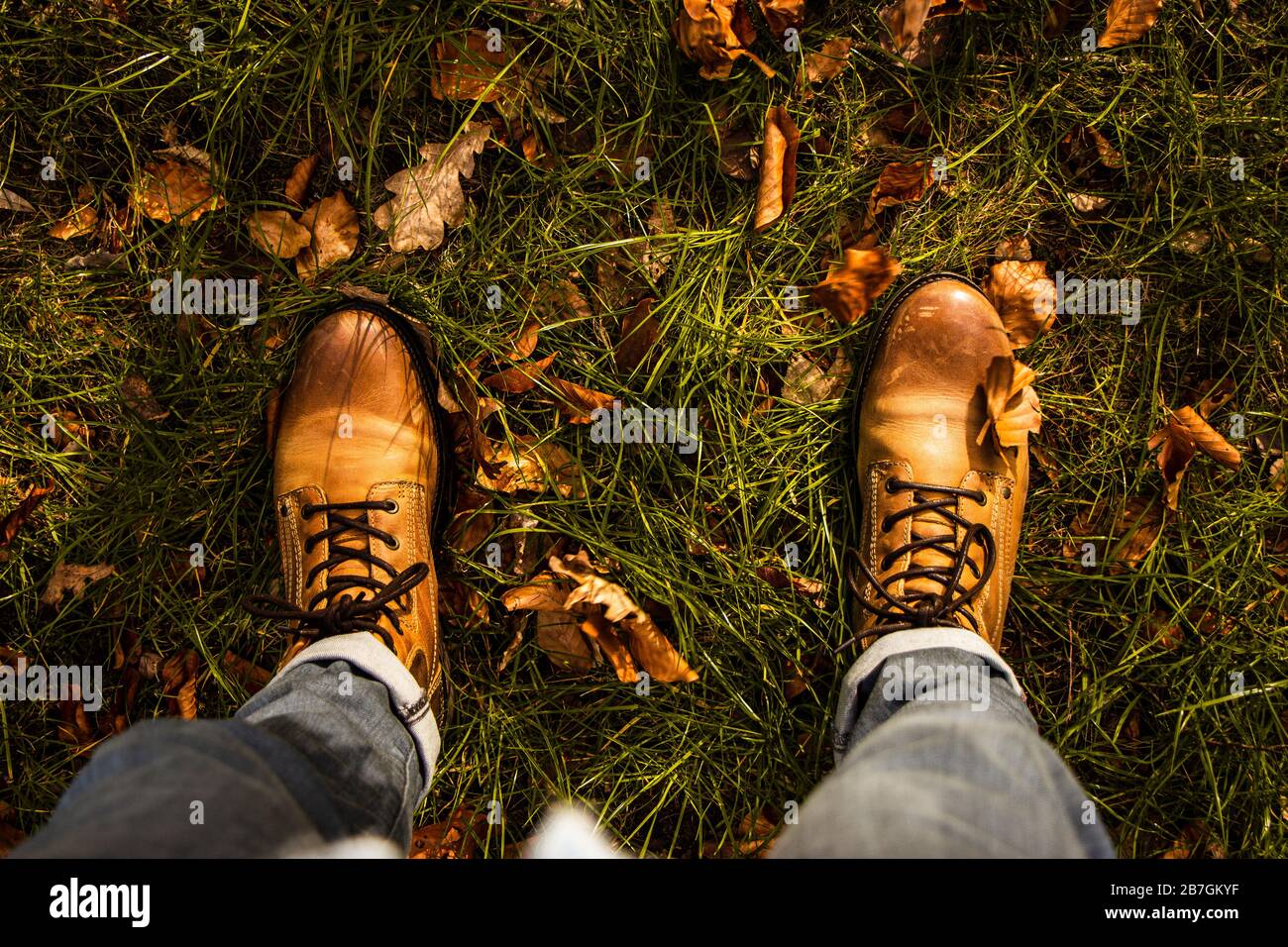 Autumn fibes top down of leather boots and rolled up trousers surrounded by grass and leaves that fell out of trees, outdoors Stock Photo