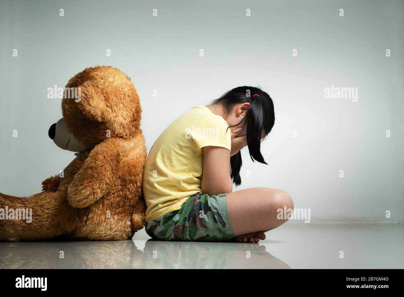 Little girl with teddy bear sitting on floor at empty room. Mental and depressed family concept. Back view Stock Photo