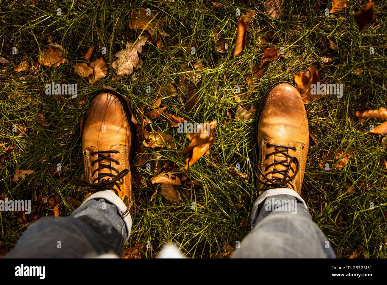 Autumn fibes top down of leather boots and rolled up trousers surrounded by grass and leaves that fell out of trees, outdoors Stock Photo