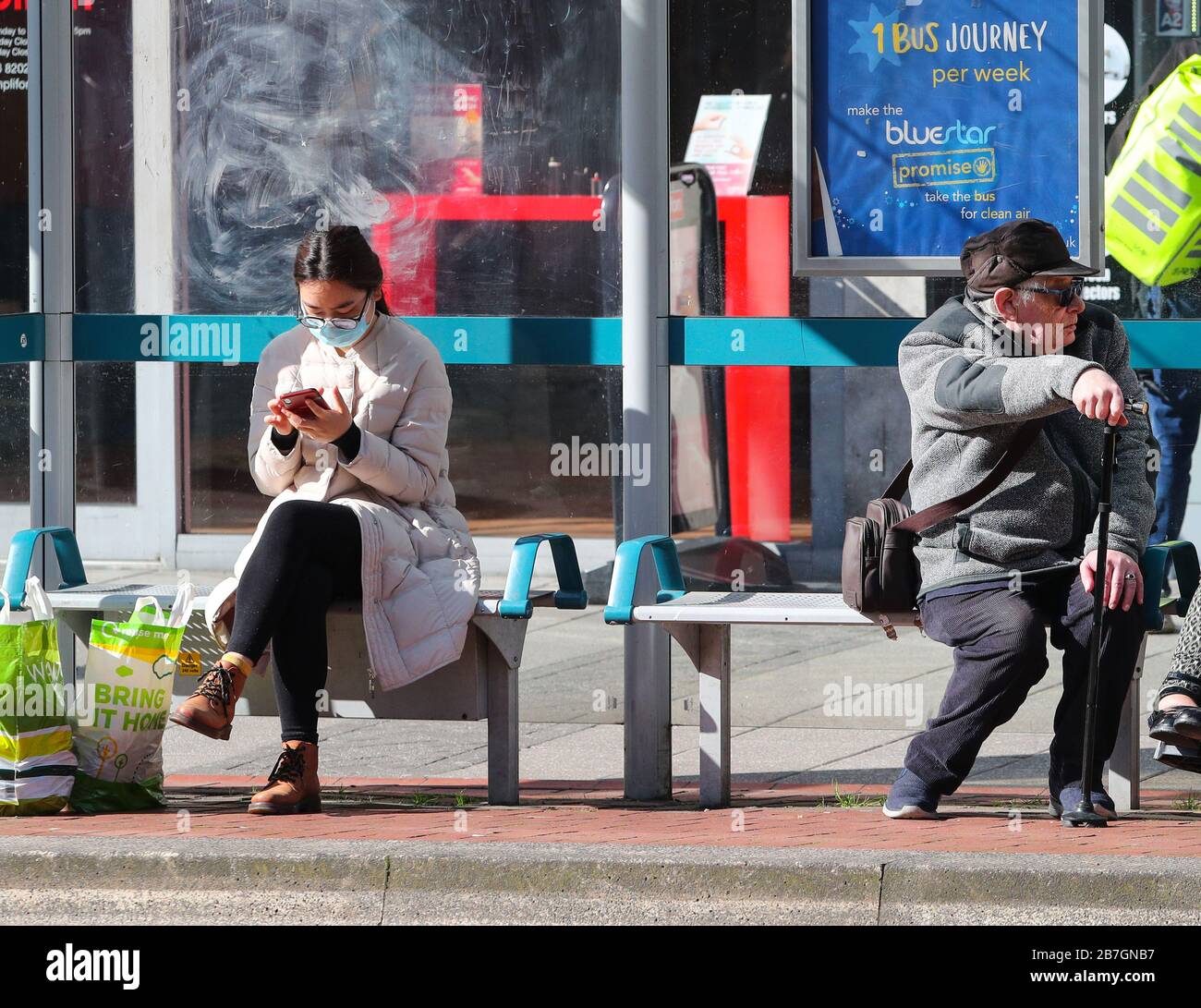 Southampton, Hampshire, UK. 16th March 2020.  A woman wearing a face mask and a pensioner keep their distance whilst waiting for a bus in Southampton. The city had it’s first confirmed case of Coronavirus over the weekend.  Credit Stuart Martin/Alamy Live News Stock Photo