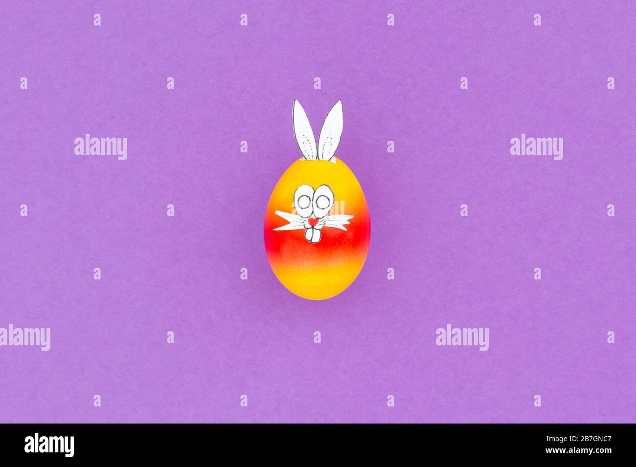 Colorful painted easter egg with funny bunny ears and cartoon face on purple background Stock Photo